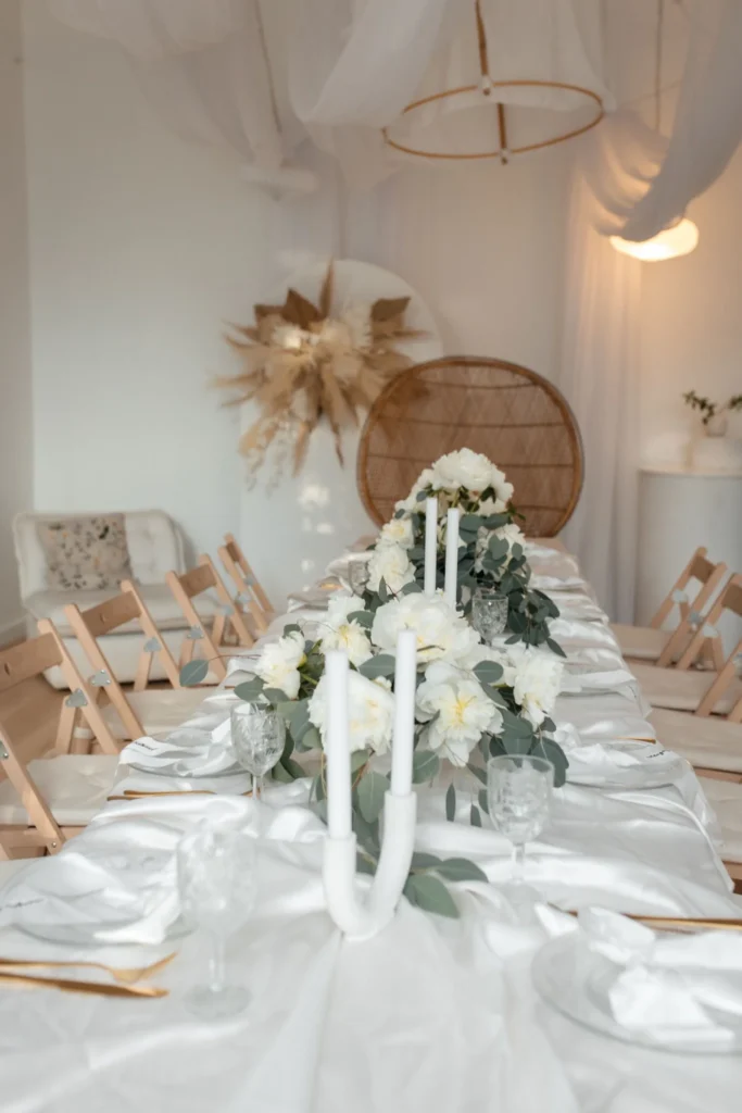 Długi stół udekorowany kwiatami i świecami w jasnym, minimalistycznym studio