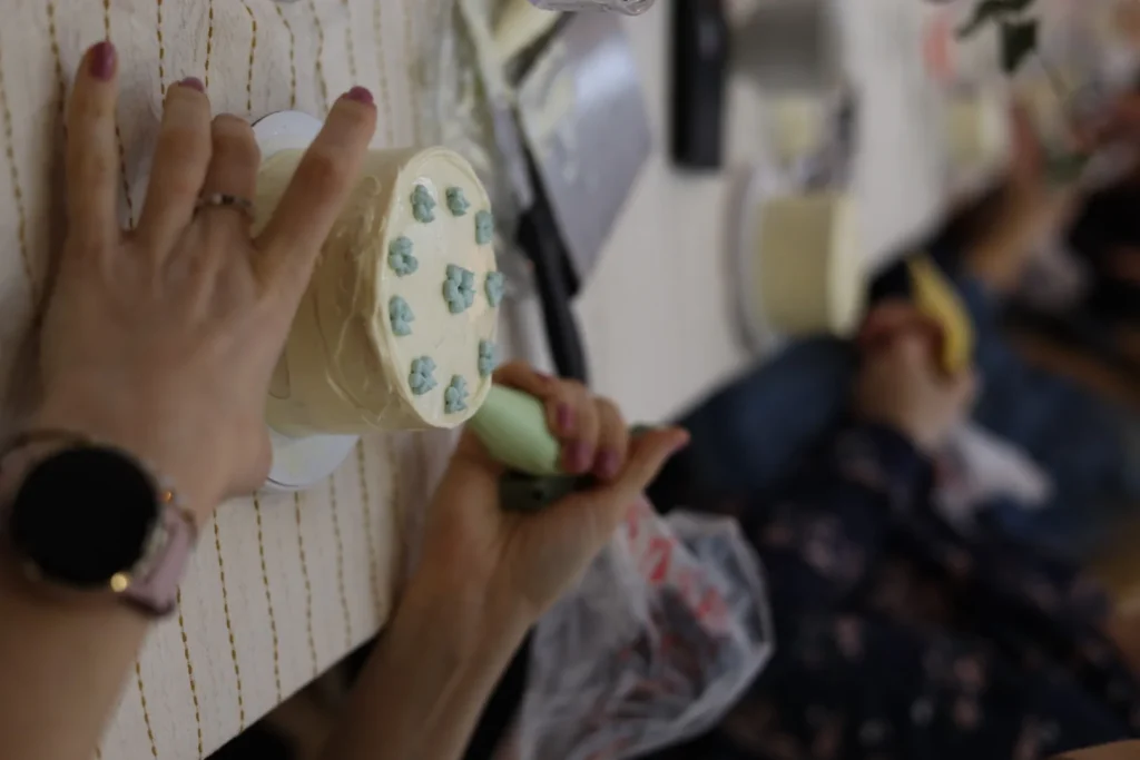 Uczestniczka warsztatów dekoruje mały tort kremem podczas kameralnych zajęć w studio