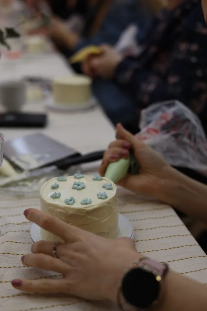 Uczestniczka warsztatów dekoruje mały tort kremem podczas kameralnych zajęć w studio