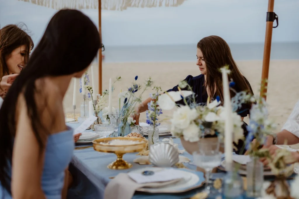 Goście przy stole podczas pikniku na plaży z kwiatową aranżacją