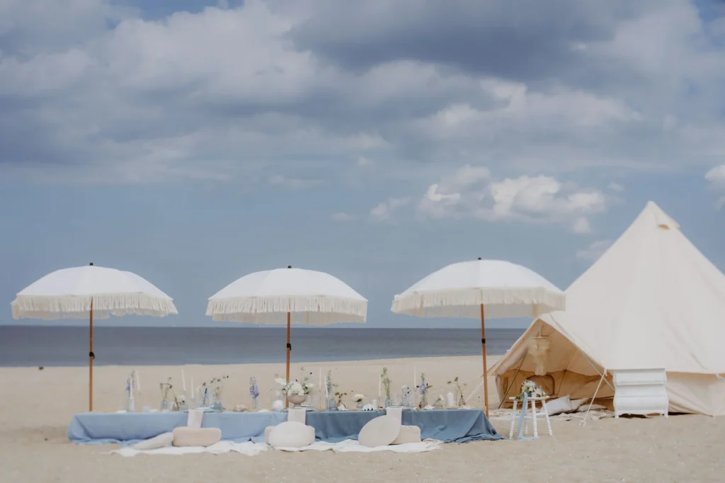 Plenerowy piknik na plaży z parasolami i namiotem w jasnej aranżacji